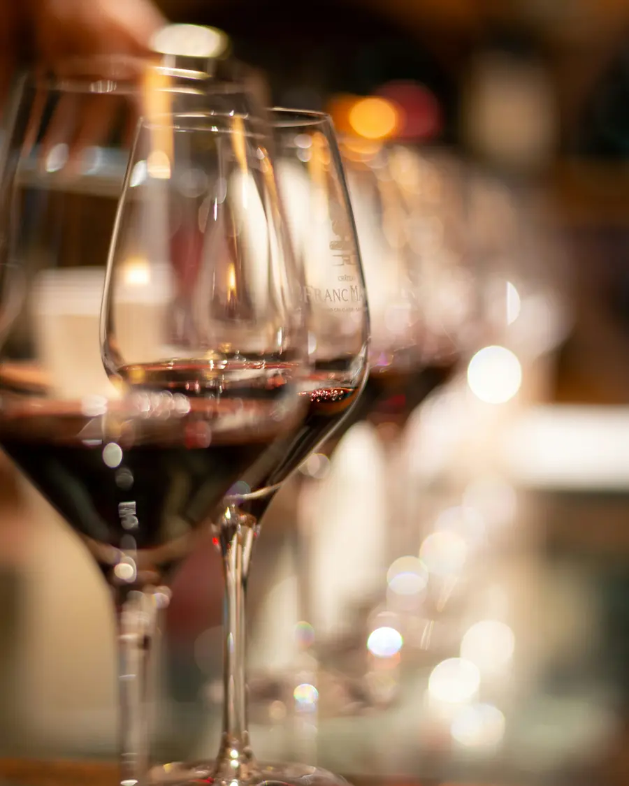 A row of filled red-wine glasses on a bar, warm light behind them.
